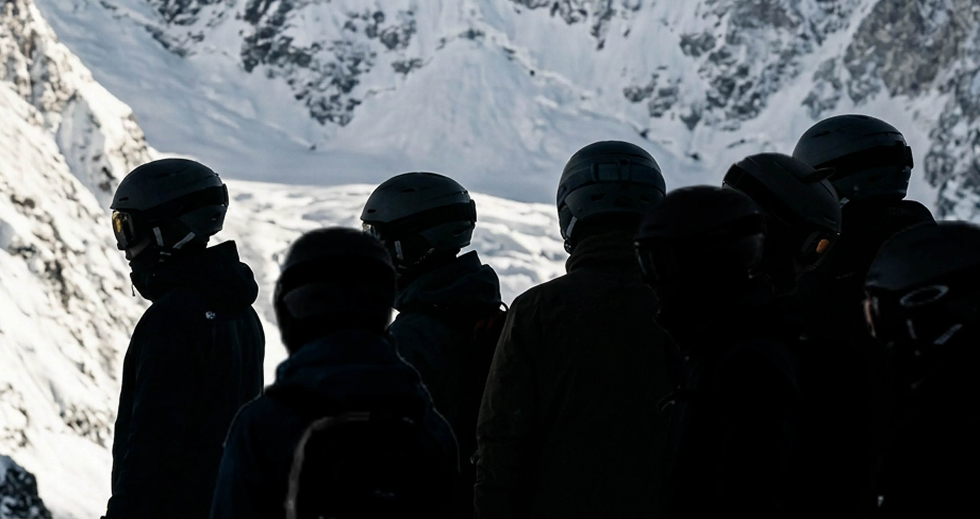 Skiers wearing helmets looking up a snowy mountain